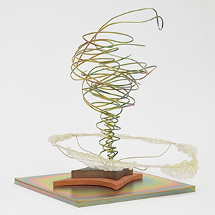 A sculptural installation featuring a colorful wire sculpture with a swirling, organic form. The sculpture is mounted on a base with a colorful, iridescent surface.